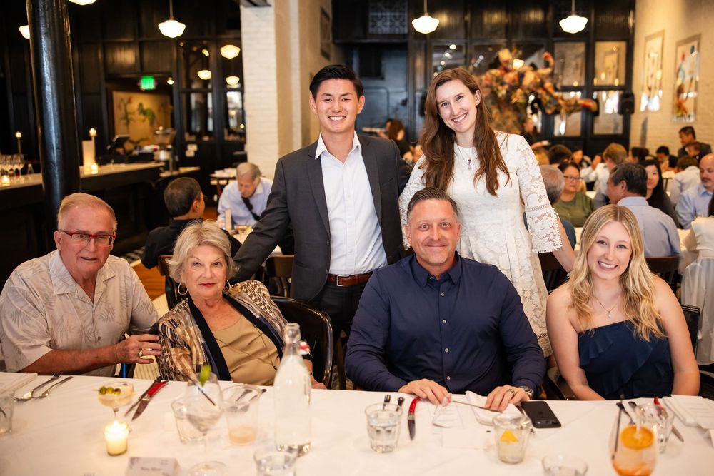 Group of six people smiling at a restaurant dinner table in an upscale dining setting.
