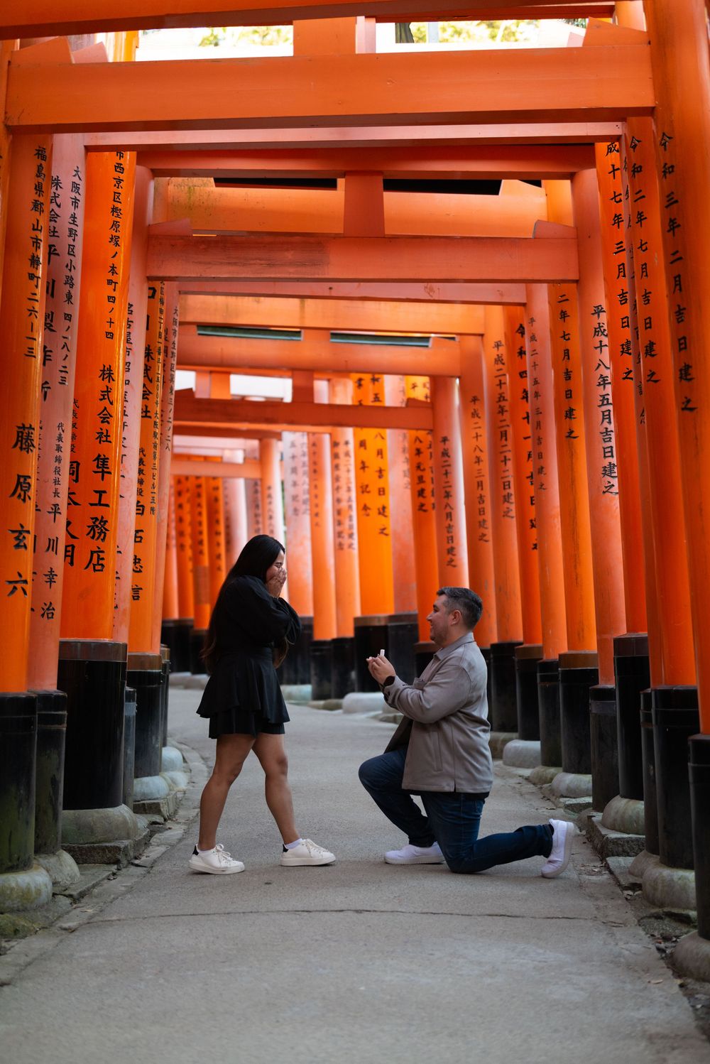 Man kneeling on one knee proposing to a woman beneath the vermilion torii gates of Fushimi Inari Shrine in Kyoto, Japan.