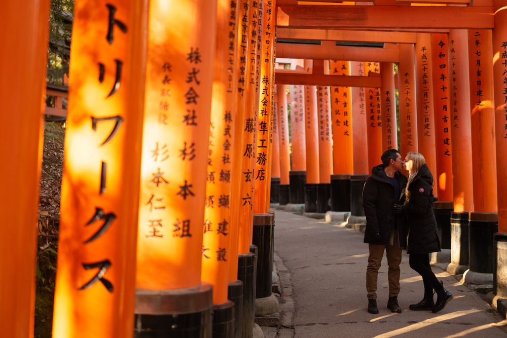 Couple walking and embracing along a path lined with vermilion torii gates at Fushimi Inari Shrine in Kyoto, Japan, in warm sunset light.