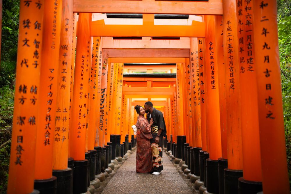 Couple in traditional attire embracing in the vermilion torii gate tunnel at Fushimi Inari Shrine in Kyoto, Japan.