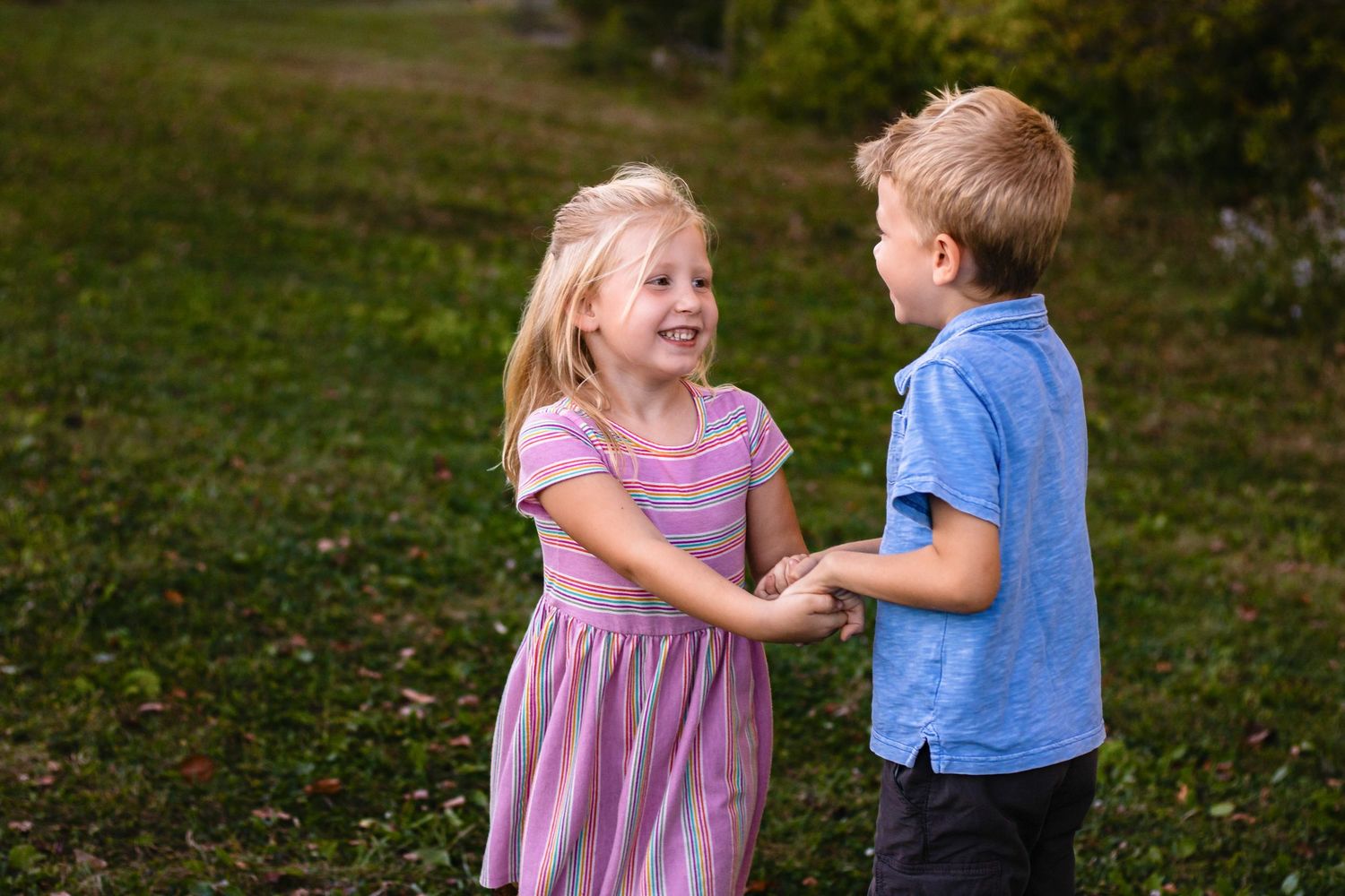 One boy and one girl playing ring around the rosie in a grass field.