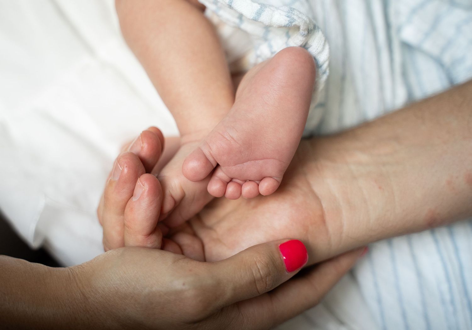 Two adult hands gently cradling tiny newborn baby feet, showcasing a tender family bonding moment.