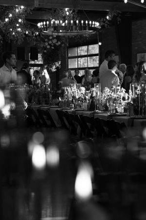 Black and white photo of an elegant candlelit wedding reception with guests mingling around a long decorated table.