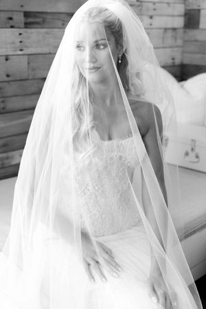 Black and white portrait of a beautiful bride wearing a lace wedding dress and flowing veil, smiling softly.