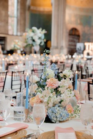 Elegant wedding reception table with blue hydrangea, peach roses, white flowers, blue taper candles, and pink napkins.