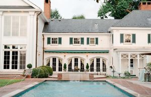 Elegant white French-style estate with green shutters, arched windows, and a rectangular outdoor swimming pool.