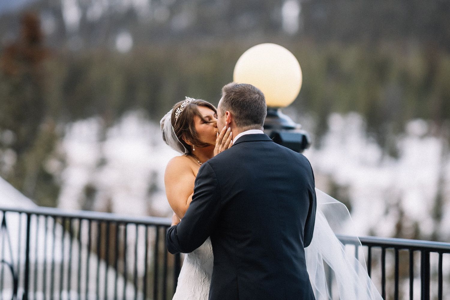 Bride and groom share a kiss beside a glowing lamp post on the terrace at their Banff winter wedding
