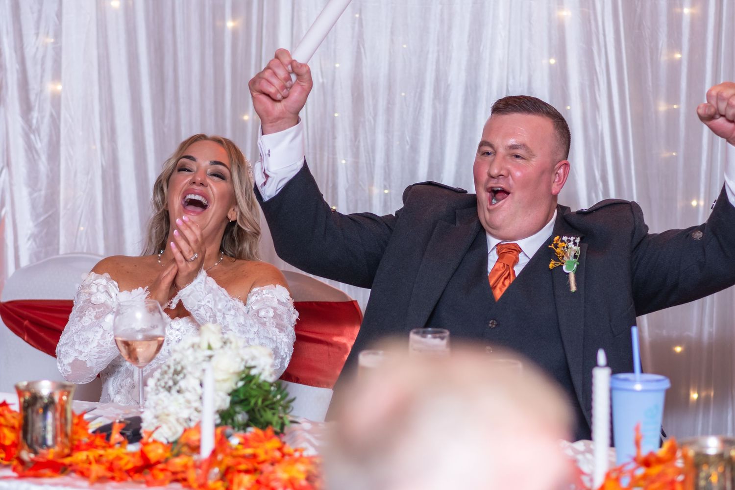 Joyful bride and groom celebrating at wedding reception, raising hands in excitement at decorated head table at Parklands, Widnes
