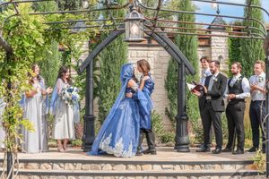 Bride and groom share first kiss in blue wedding gown at outdoor garden ceremony with wedding party.