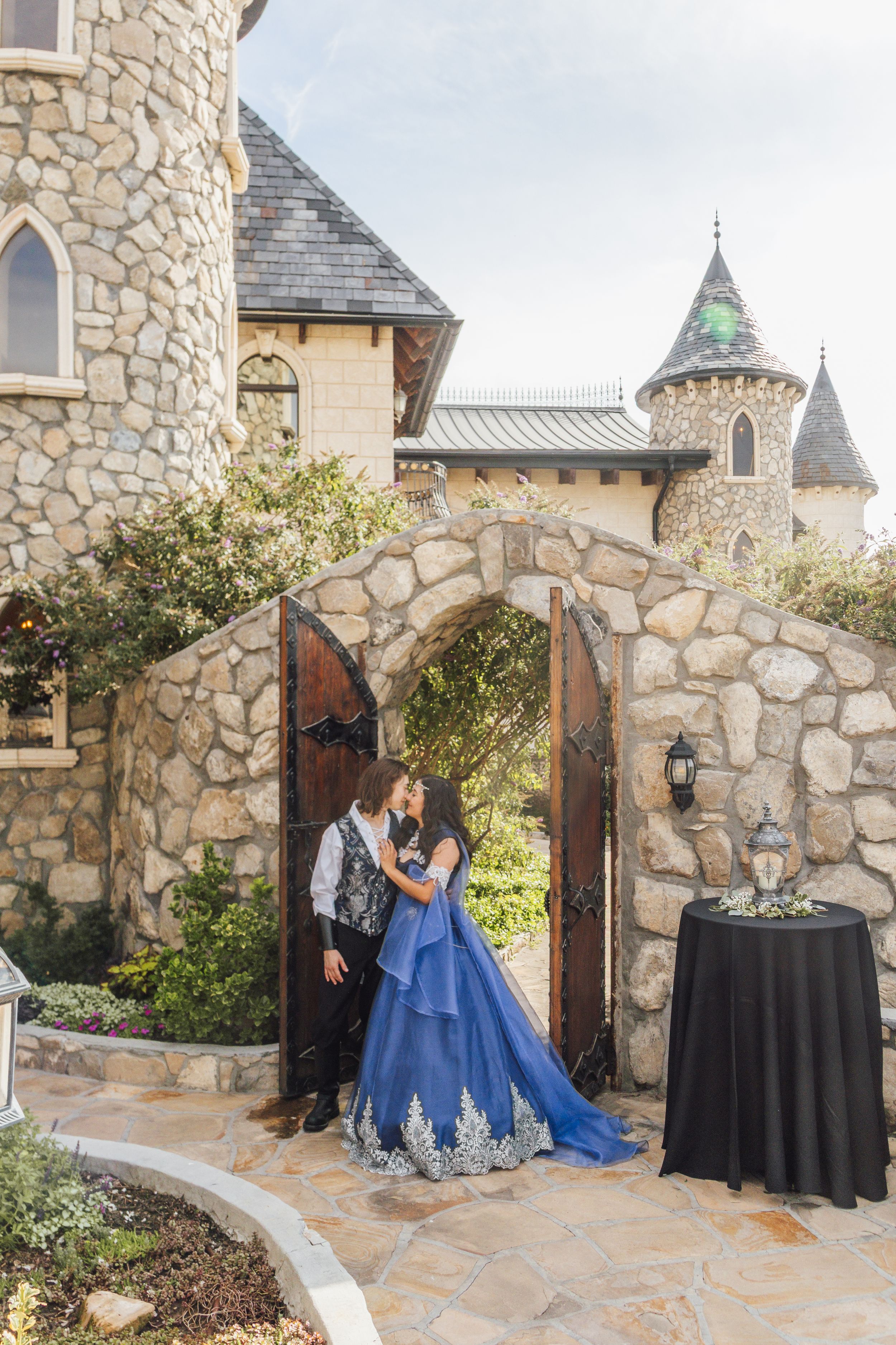 Couple in elegant attire sharing a romantic moment under a stone archway at a castle venue.