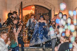 Bride in blue gown and groom exit venue amid bubbles and cheering guests at elegant wedding celebration.