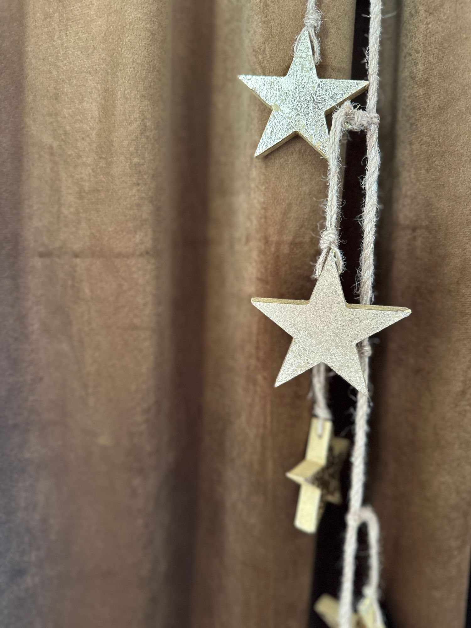 Rustic wooden star garland hanging on twine against a brown curtain backdrop, perfect for holiday decor.