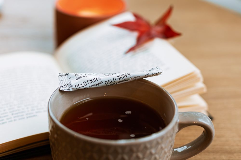 Stick de collagène Oslo Skin Lab posé sur une tasse de thé dans une ambiance automnale avec livre et bougie
