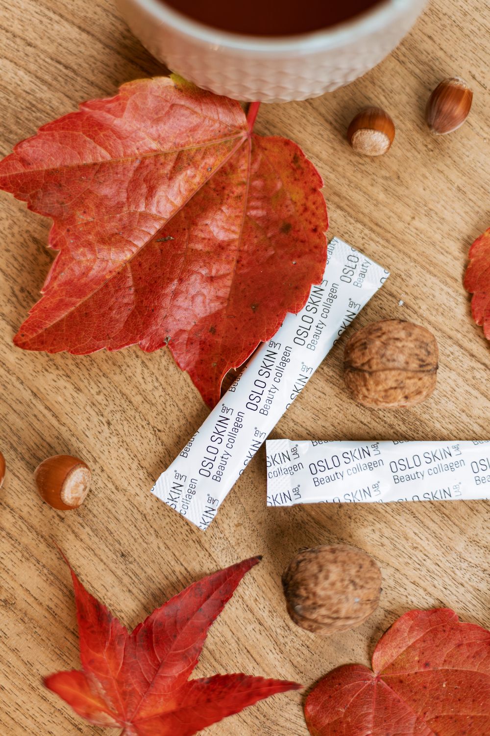 Sticks de collagène Oslo Skin Lab posés sur une table avec des noisettes, des noix et des feuilles aux couleurs automnales