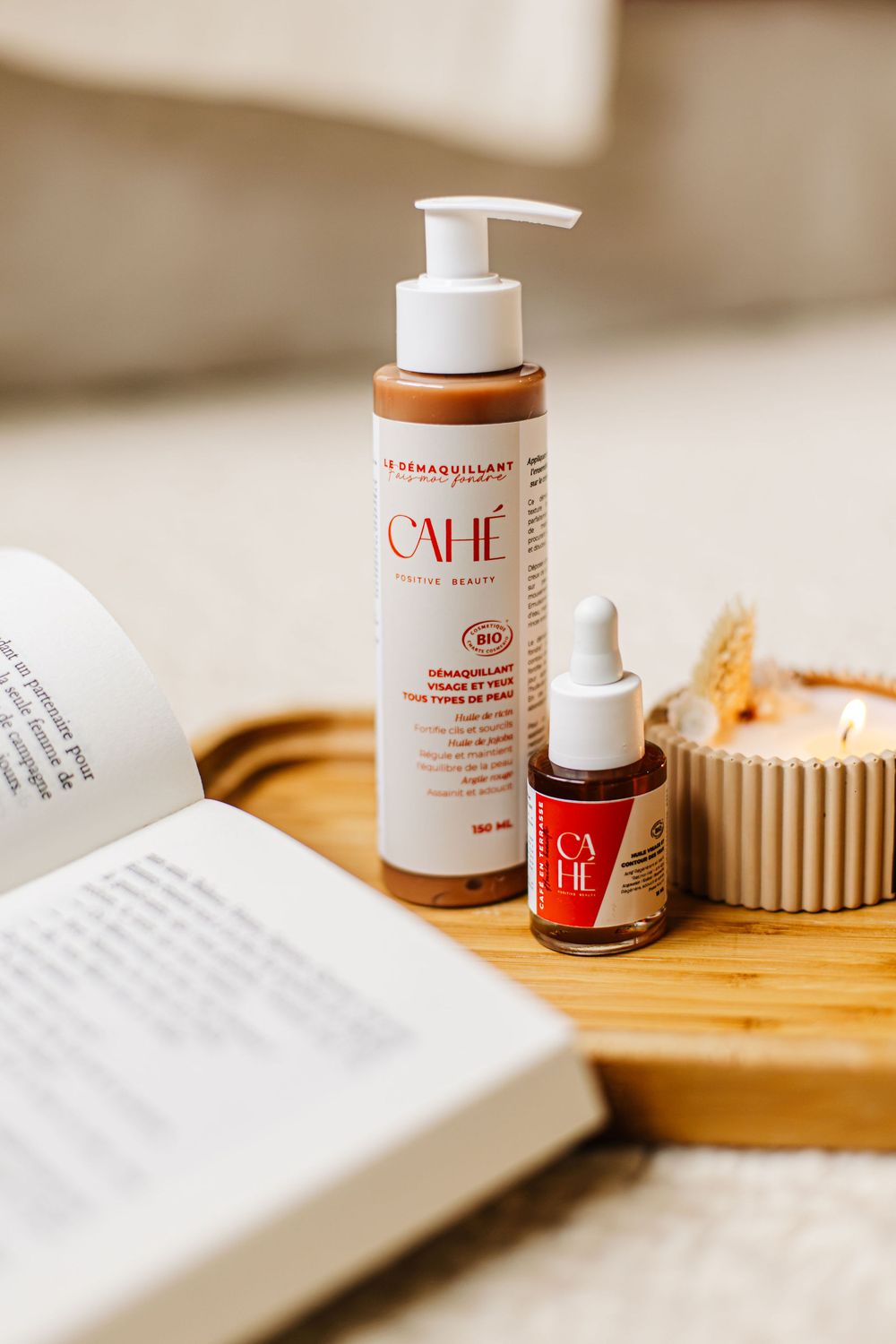 Produits Cahé Cosmetics posés sur un plateau avec une bougie allumée et un livre ouvert