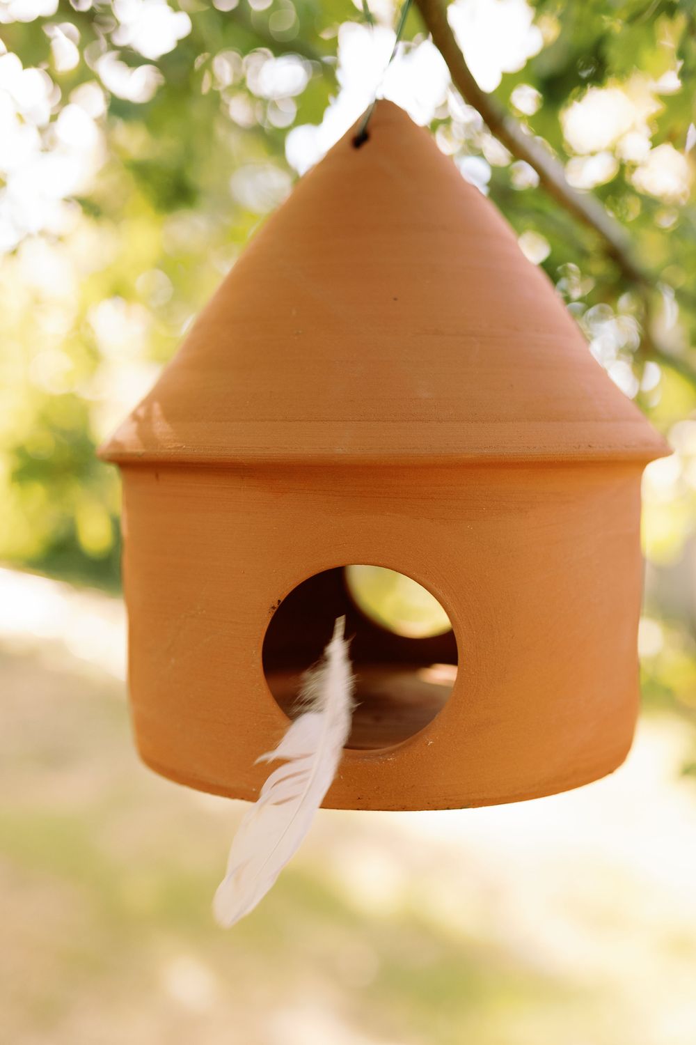 Abri à oiseaux de la marque Potterie Lutton représenté avec une plume qui vole devant l'abri