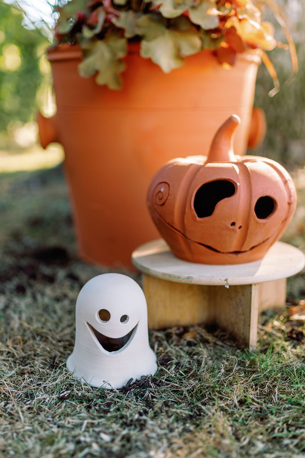 Citrouille, fantôme et gros pot de la marque Potterie Lutton disposés dans un jardin avec des feuilles automnales