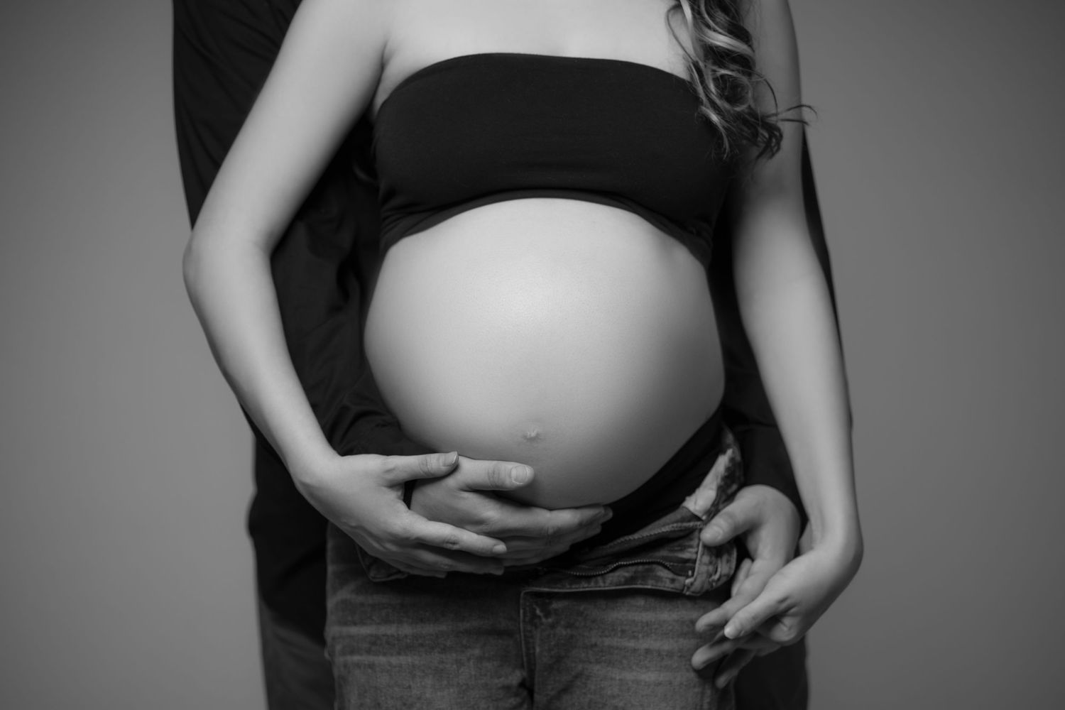 Black-and-white maternity portrait of a couple embracing and holding a baby bump.