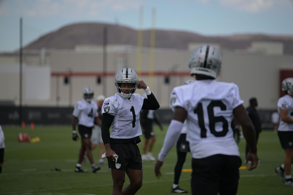 Football players in white jerseys and helmets, numbers 1 and 16, warm up on a practice field with mountains in the background.