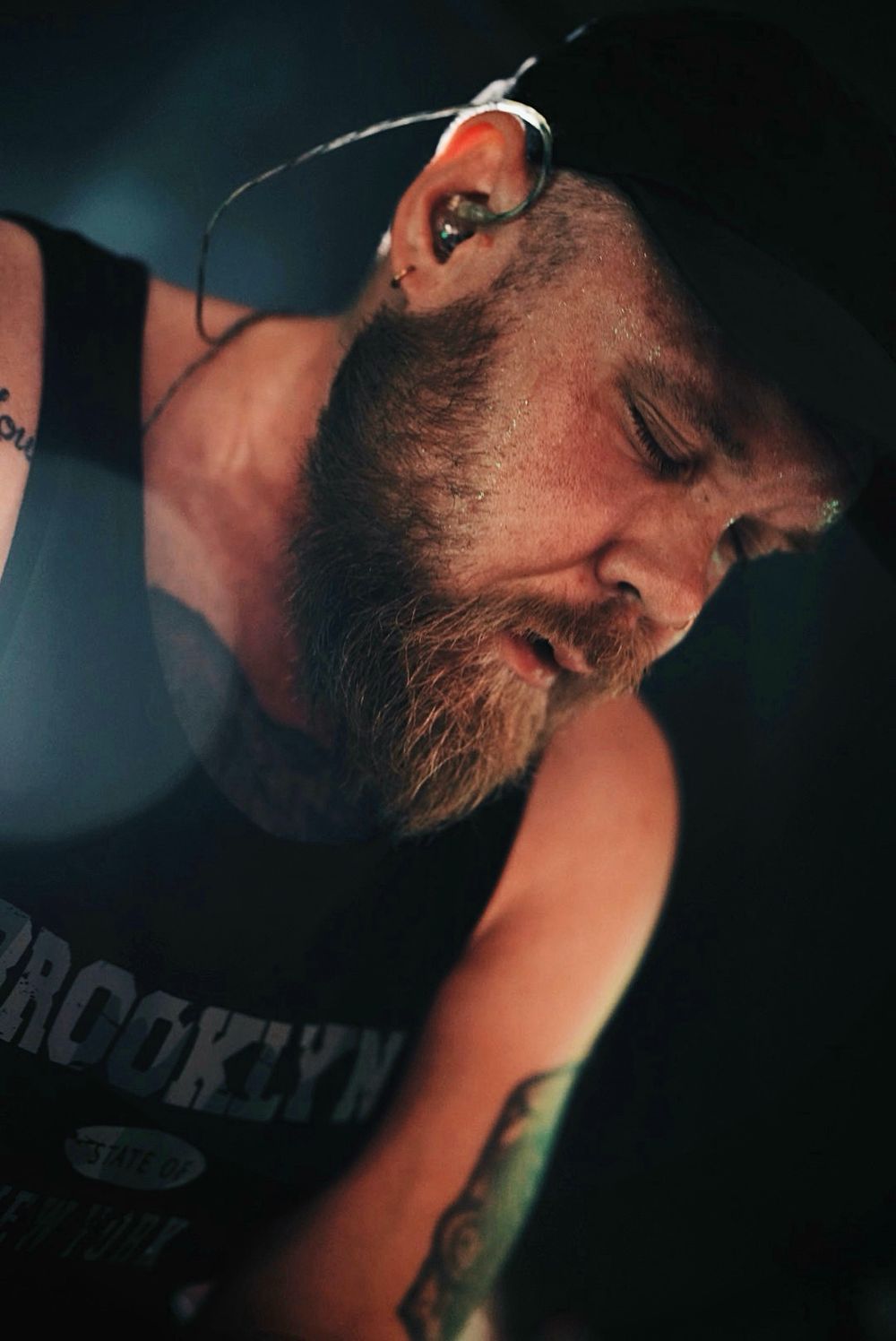 Close-up of Arvid Hällagård musician with beard performing on stage wearing a Brooklyn shirt and baseball cap.