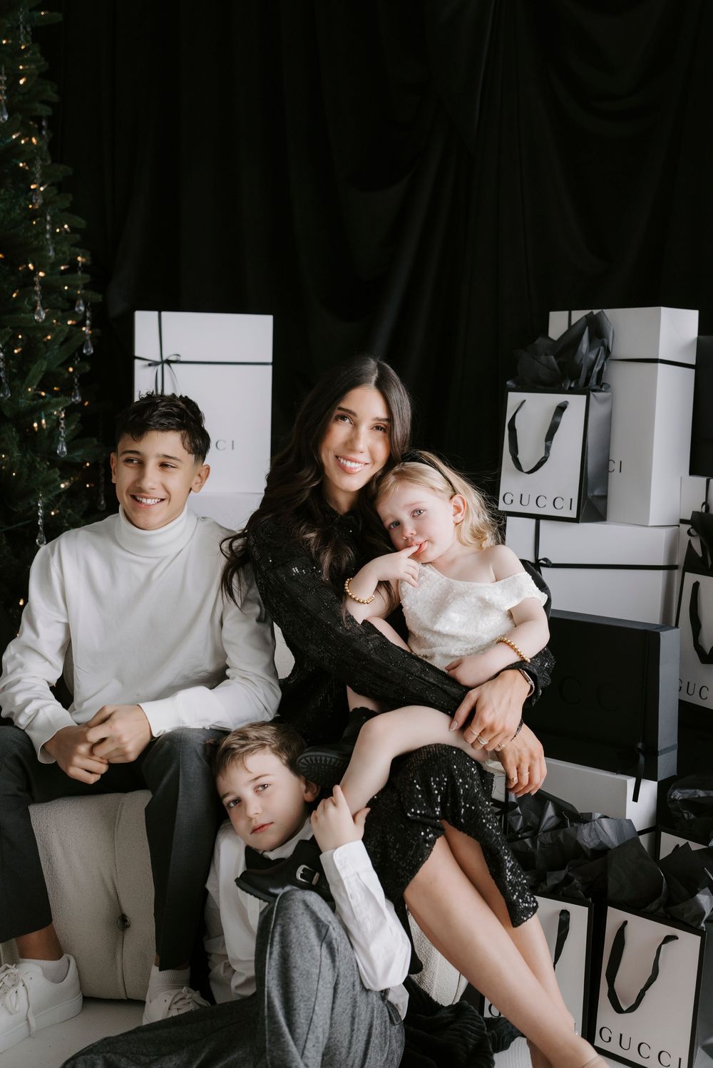 A woman and three children pose happily near a Christmas tree surrounded by Gucci shopping bags and white gift boxes.