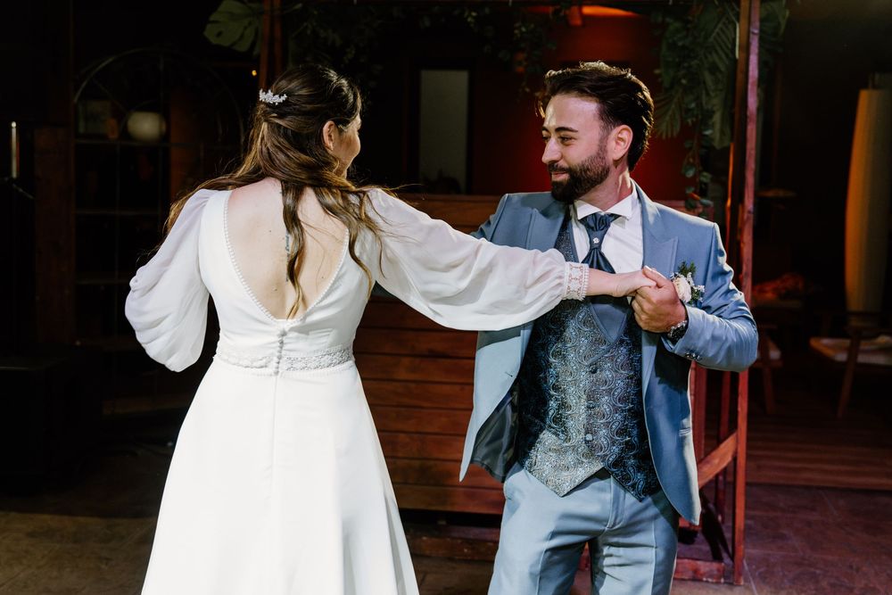 Bride in a white gown and groom in a blue suit share a first dance at their wedding reception.