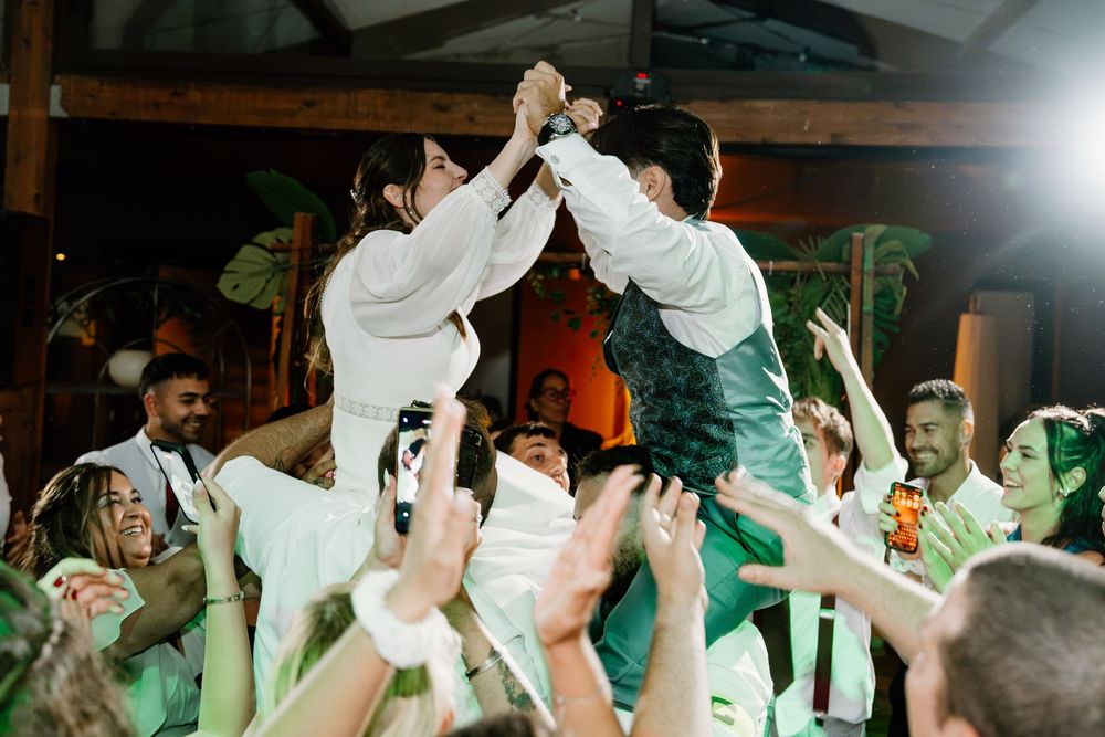 Wedding guests cheer and raise their hands as the bride and groom are lifted high in celebration on the dance floor.