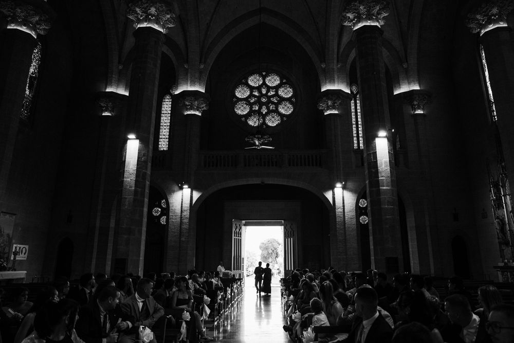 Black and white photo of a couple silhouetted in a church doorway, with guests seated in pews and a rose window above.