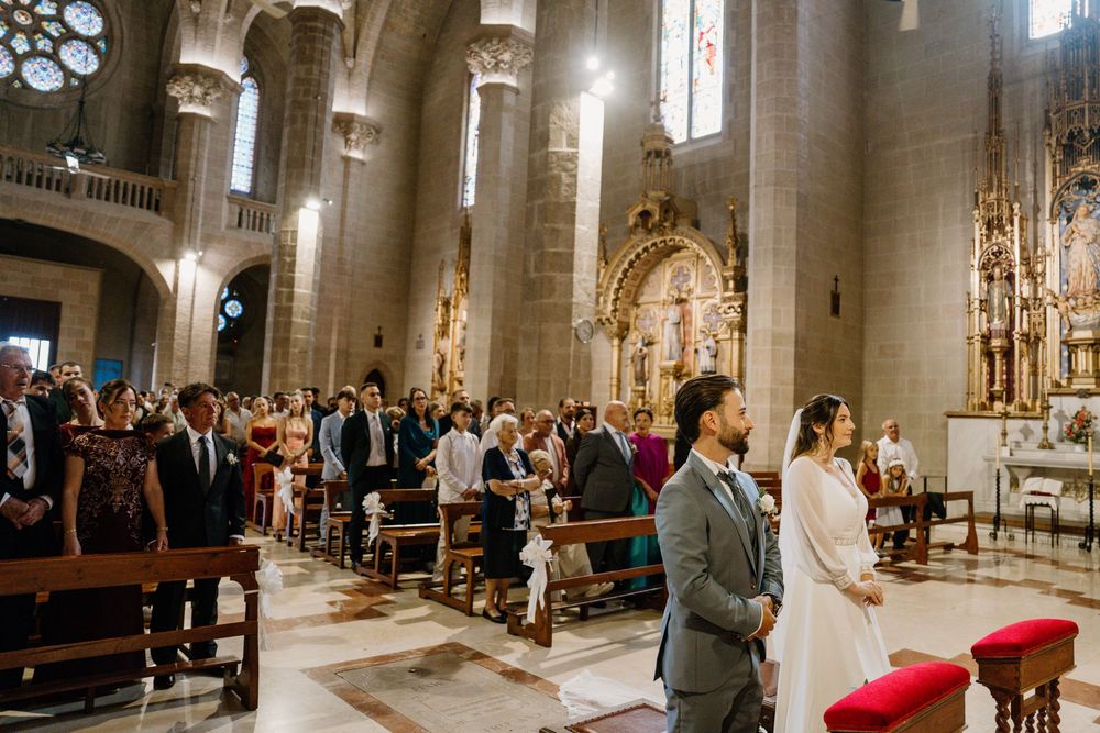 Bride and groom walk down the aisle of a grand cathedral during a wedding ceremony as guests watch from the wooden pews.