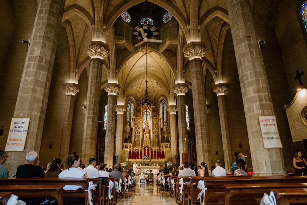 Guests seated in wooden pews fill a grand Gothic church interior with ribbed vaults, stone columns, and a glowing golden altar.