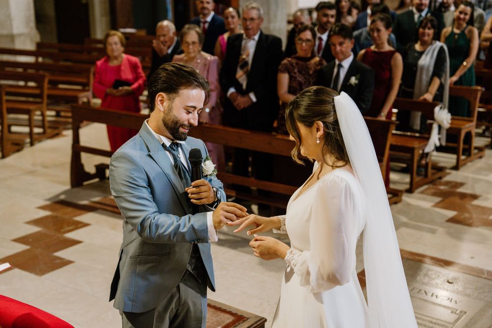 Bride and groom exchange rings during a church wedding ceremony while seated guests look on in the pews.