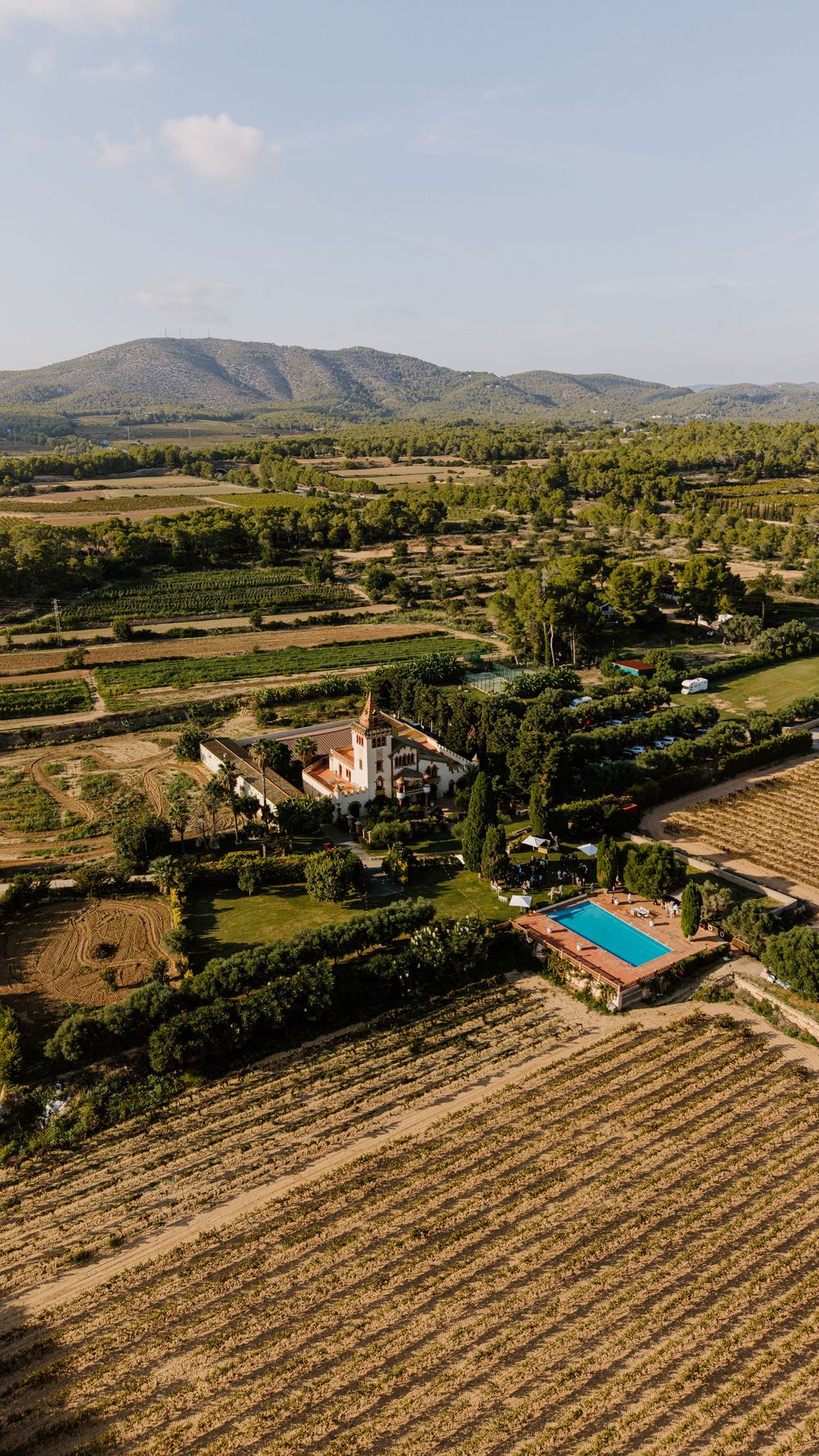 Aerial view of a countryside estate with a pool, surrounded by vineyards and farmland, with rolling mountains in the distance.