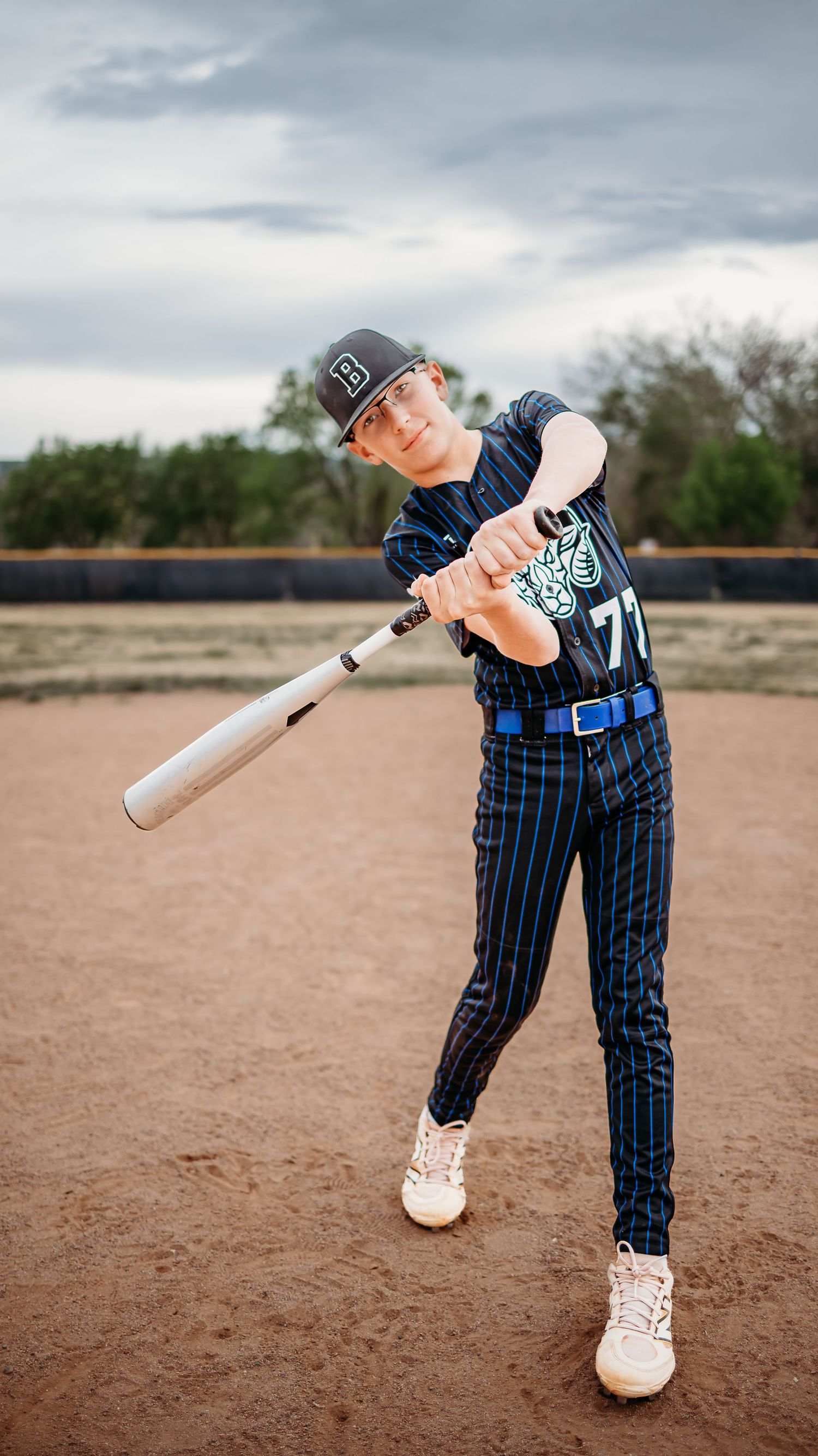 A baseball player in a pinstripe uniform and cap mid-swing with a white bat on a dirt infield field during a team photo session.