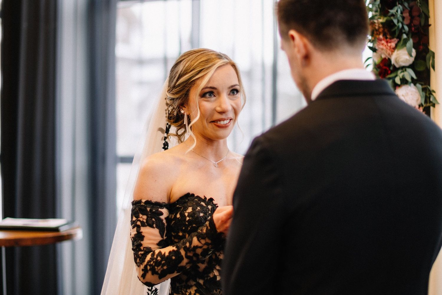 Bride in black lace smiling up at her groom during their vows at Mainspace in Canmore