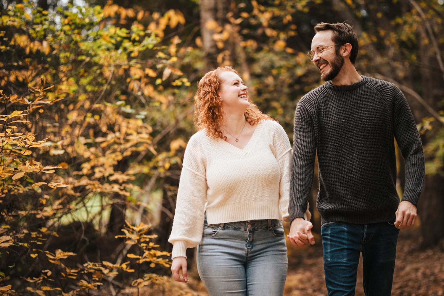 Engaged couple laughing while walking hand in hand through the forest at Borderland State Park