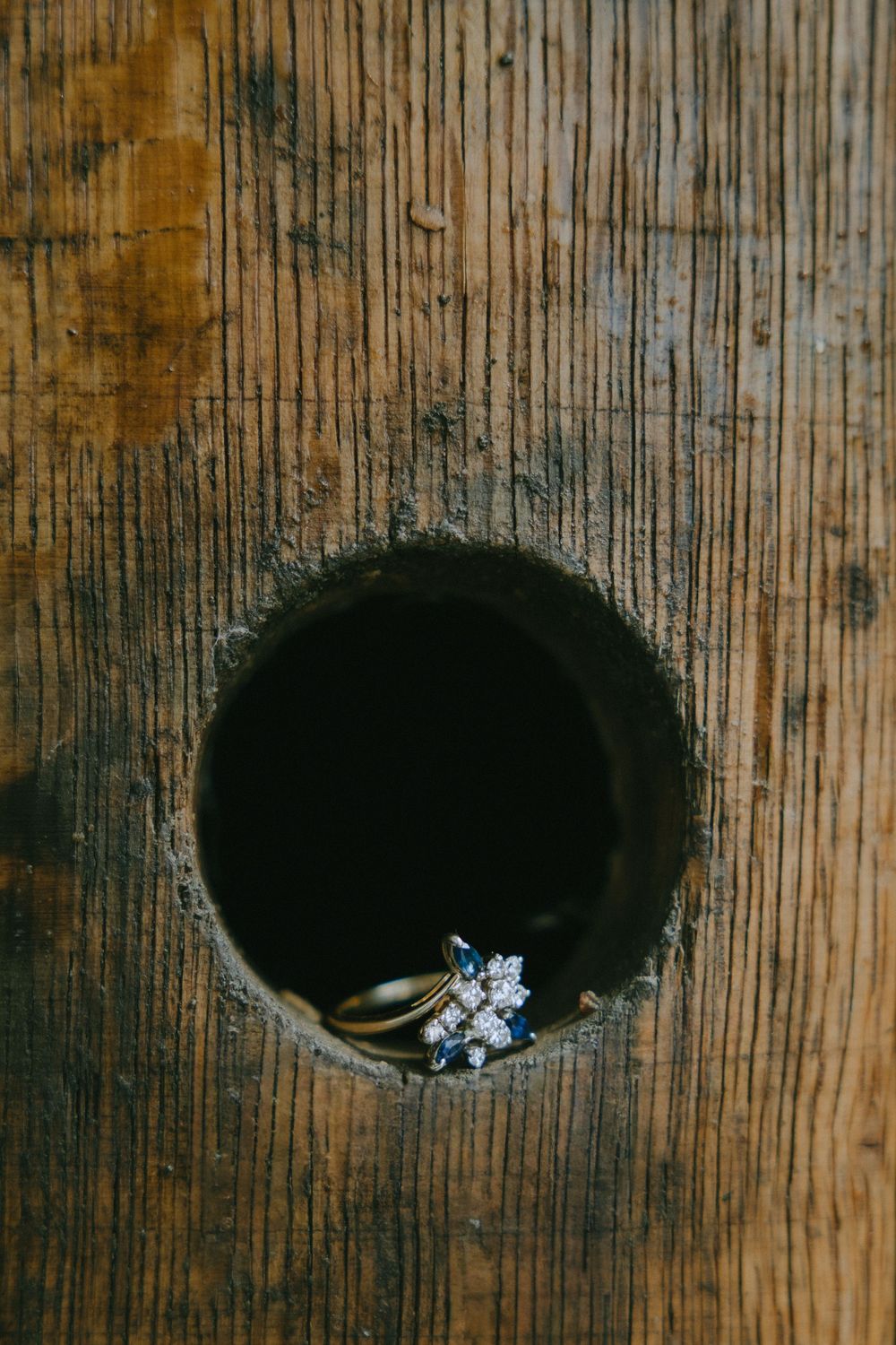 Gold ring with blue sapphire and diamond cluster displayed in a rustic wooden knot hole, perfect for vintage jewelry.