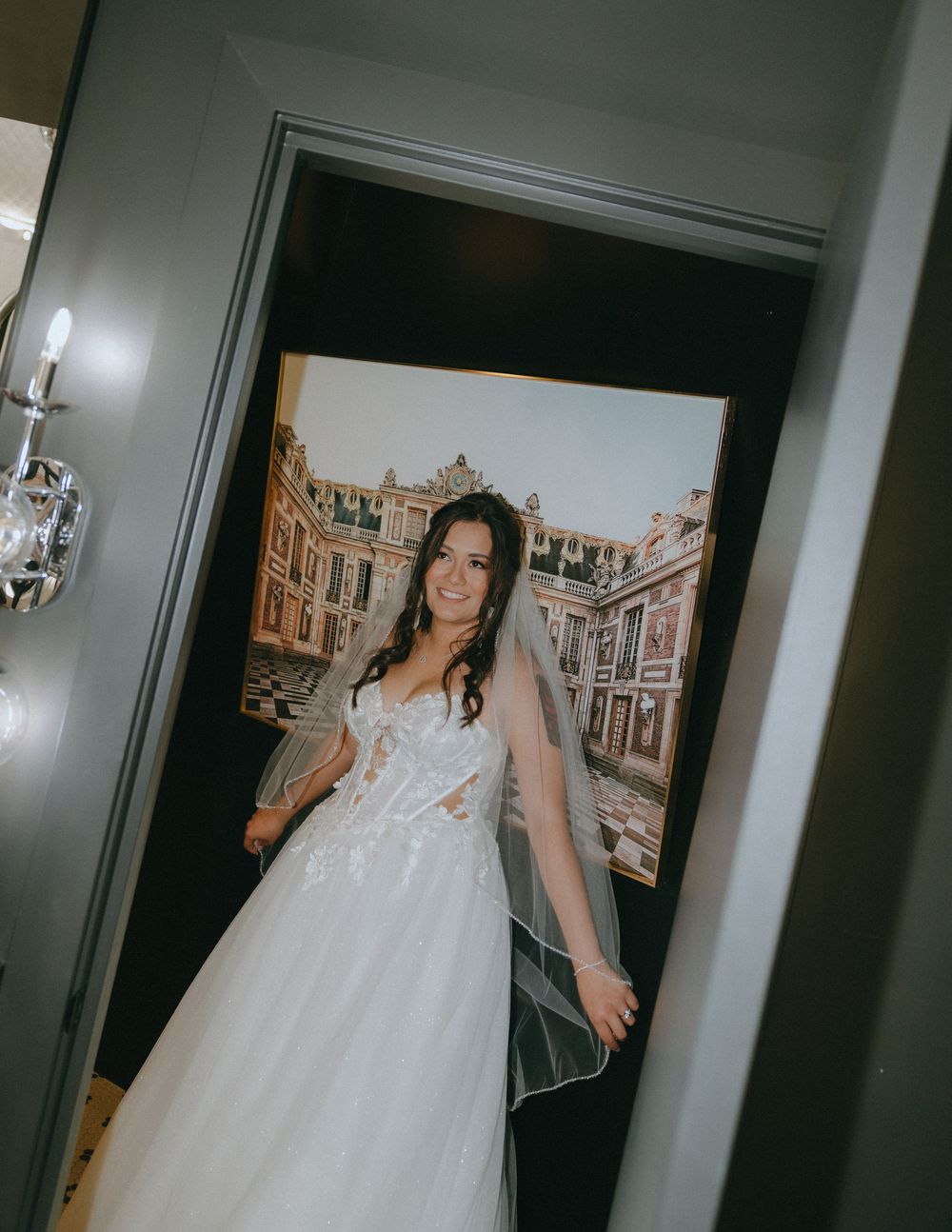Bride in a lace ball gown wedding dress and veil smiling in a doorway.