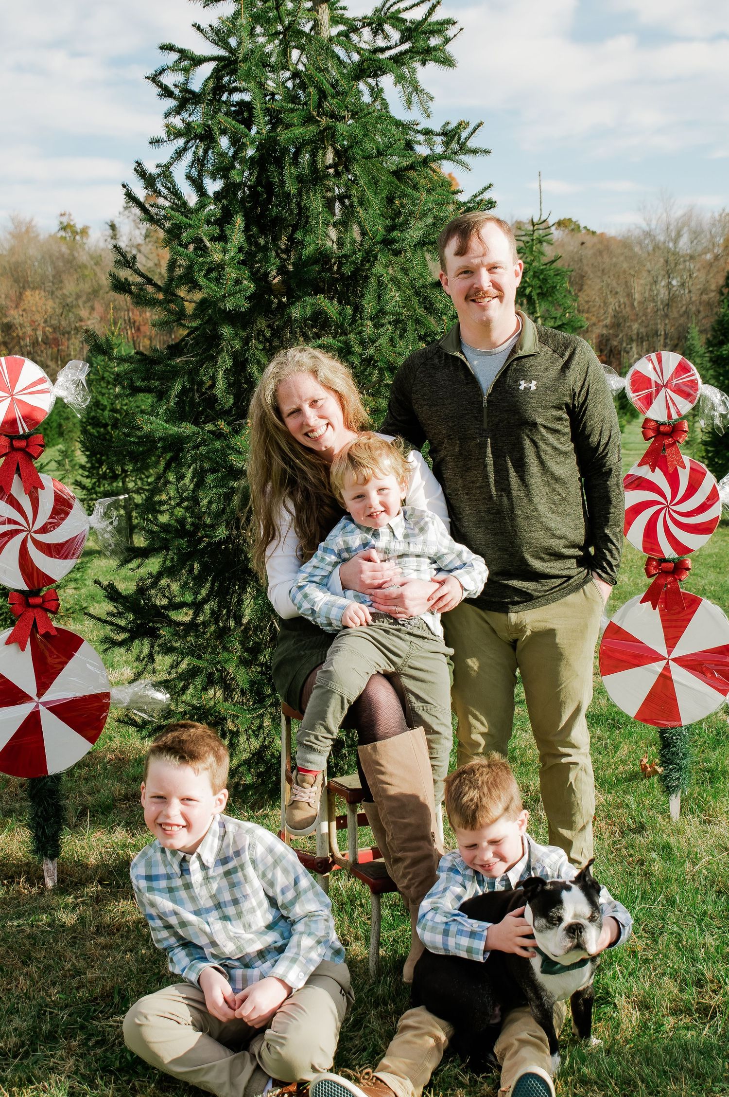 Family of five with a dog posing in front of a Christmas tree with peppermint decorations outdoors.
