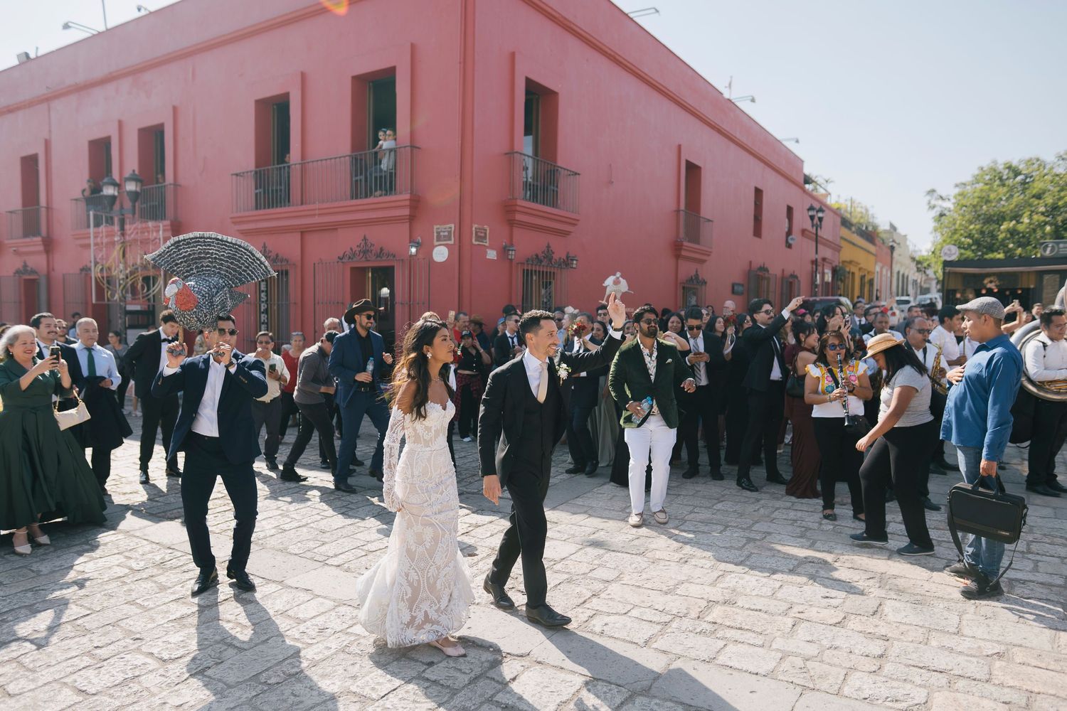 Bride and groom walk hand-in-hand through cobblestone streets of Oaxaca, Mexico, surrounded by wedding guests.
