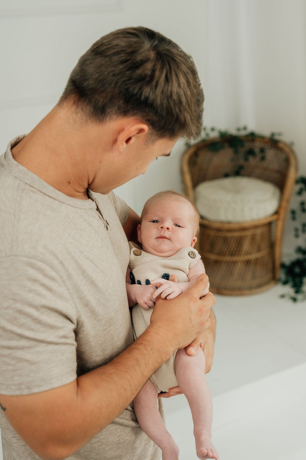 A young father tenderly holds his newborn baby in a bright, minimalist nursery room.