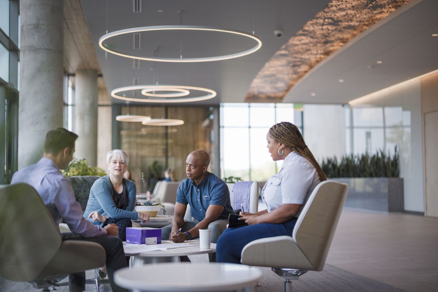 Diverse business professionals having a meeting in a modern corporate lobby with circular pendant lights.