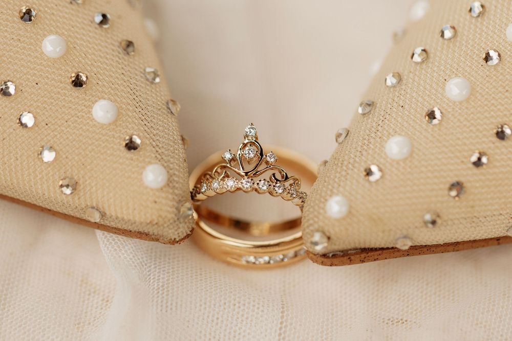 Gold wedding bands and diamond crown ring displayed on pearl-embellished ivory fabric for elegant bridal jewelry.