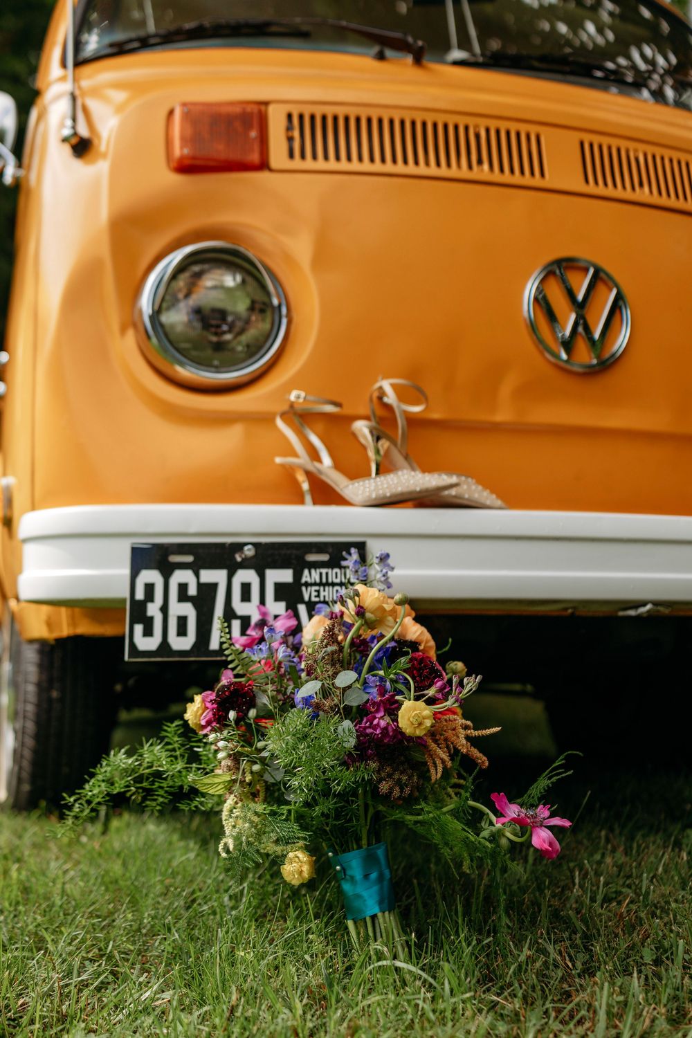 Vibrant wildflower bridal bouquet and heels in front of classic orange Volkswagen van with antique vehicle plate.