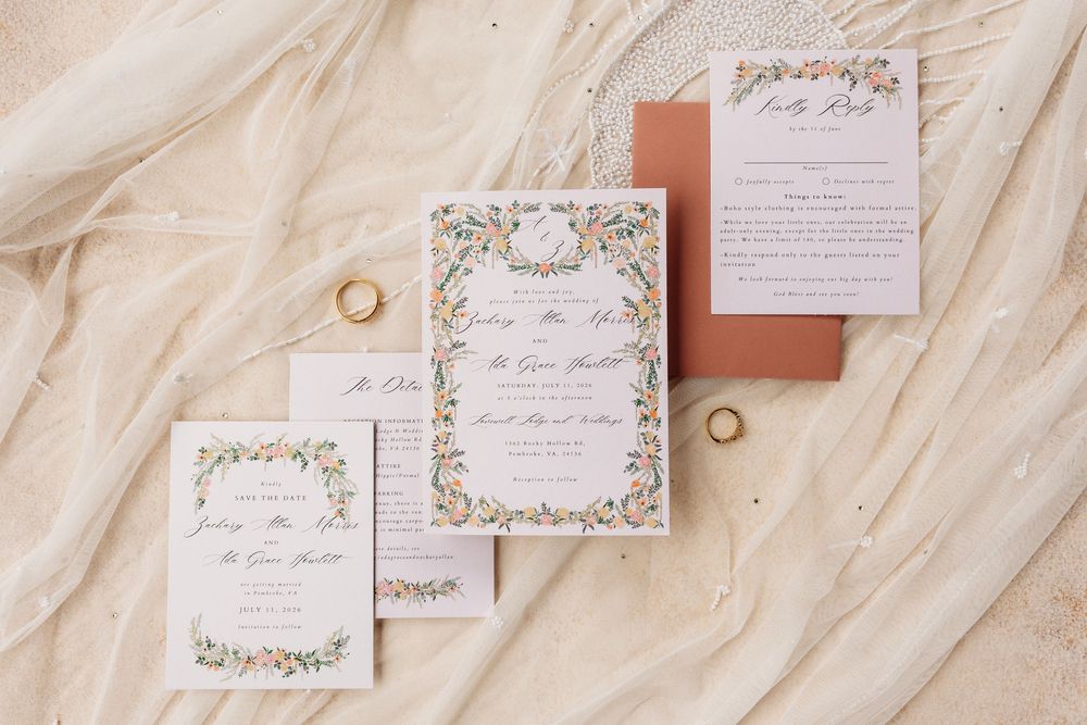 Elegant wedding invitation suite with floral borders, RSVP card, and gold rings on a soft ivory fabric backdrop.