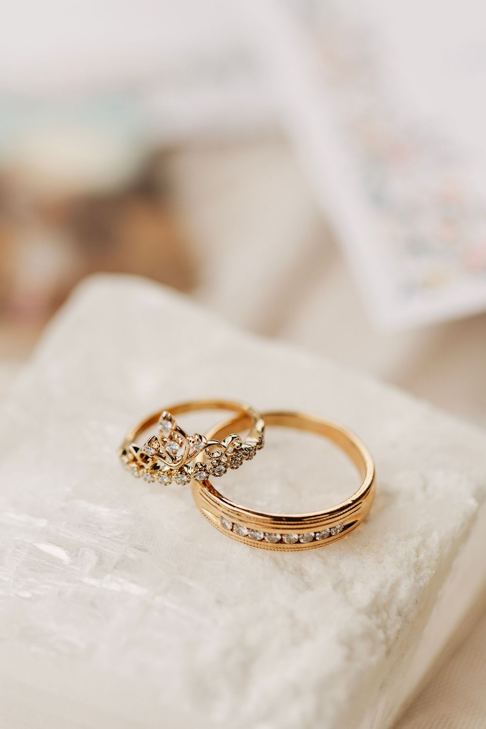 Two gold rings with diamonds, one crown-shaped, resting on a white surface.