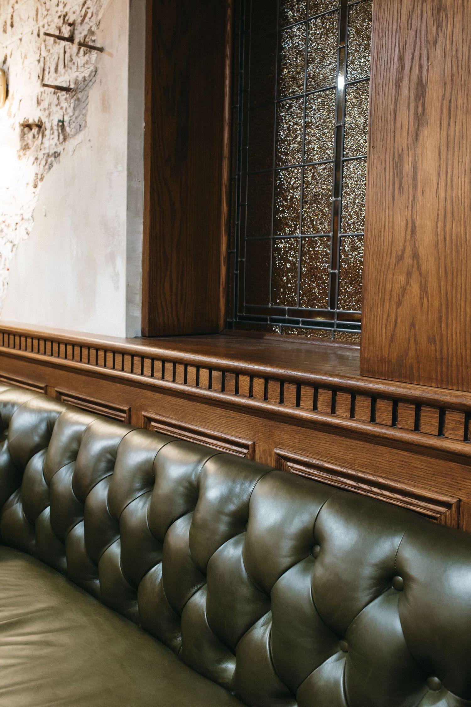 Green tufted leather booth seating against wooden paneling in an upscale restaurant interior.