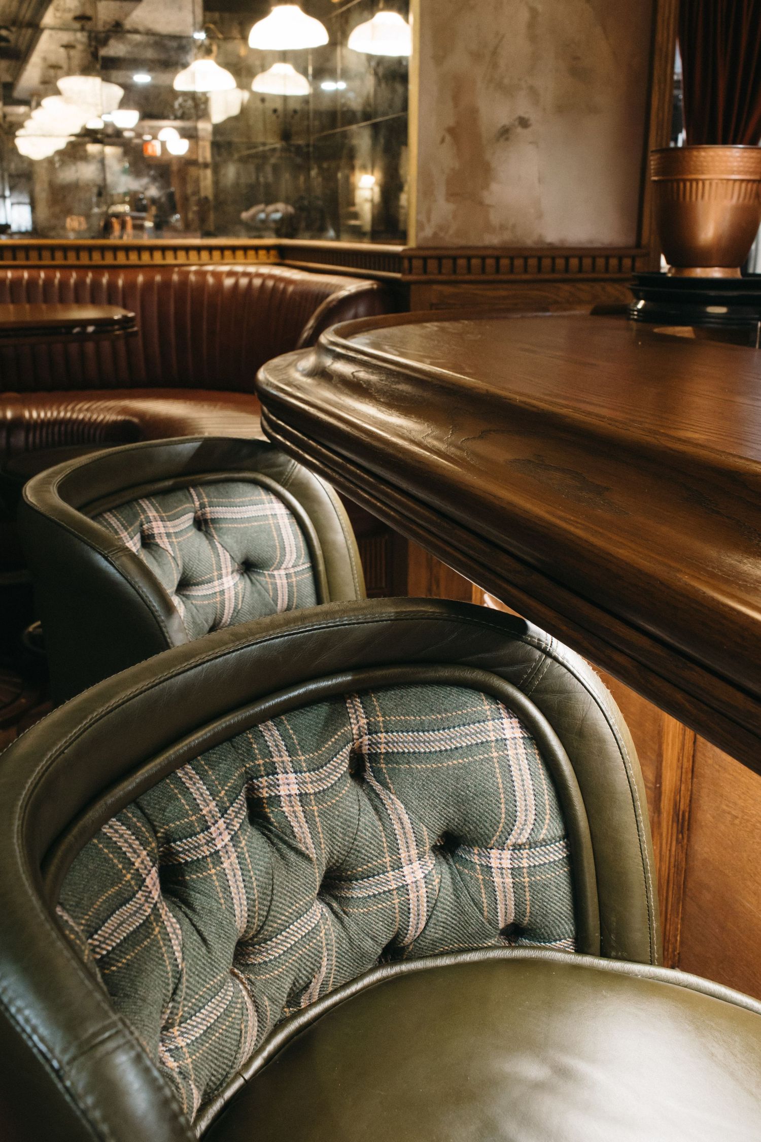 Elegant bar seating with tufted plaid fabric chairs and rich wooden counter in a vintage-style restaurant interior.