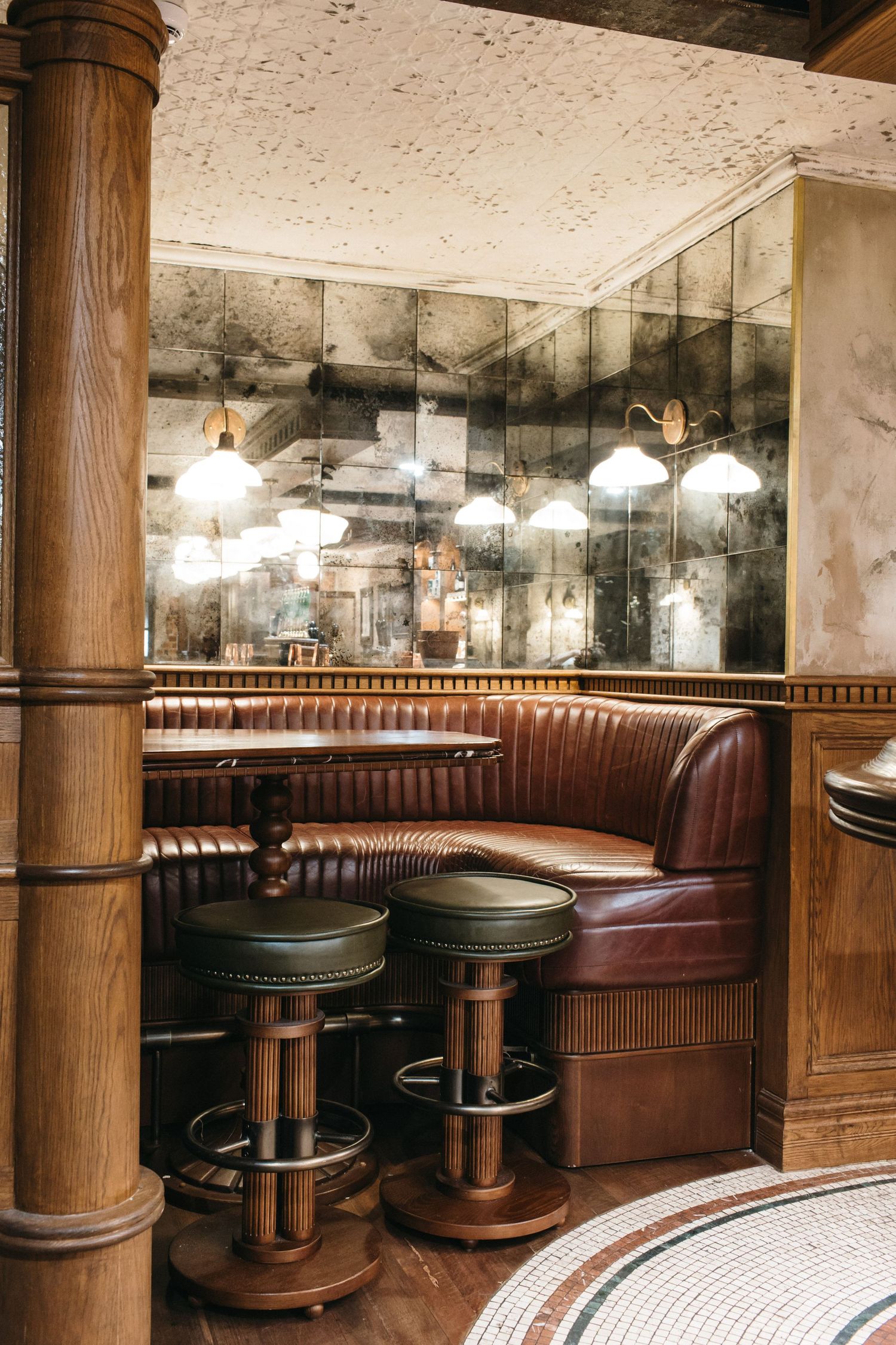 Vintage restaurant booth with tufted leather seating, wooden stools, antique mirrors, and warm pendant lights.