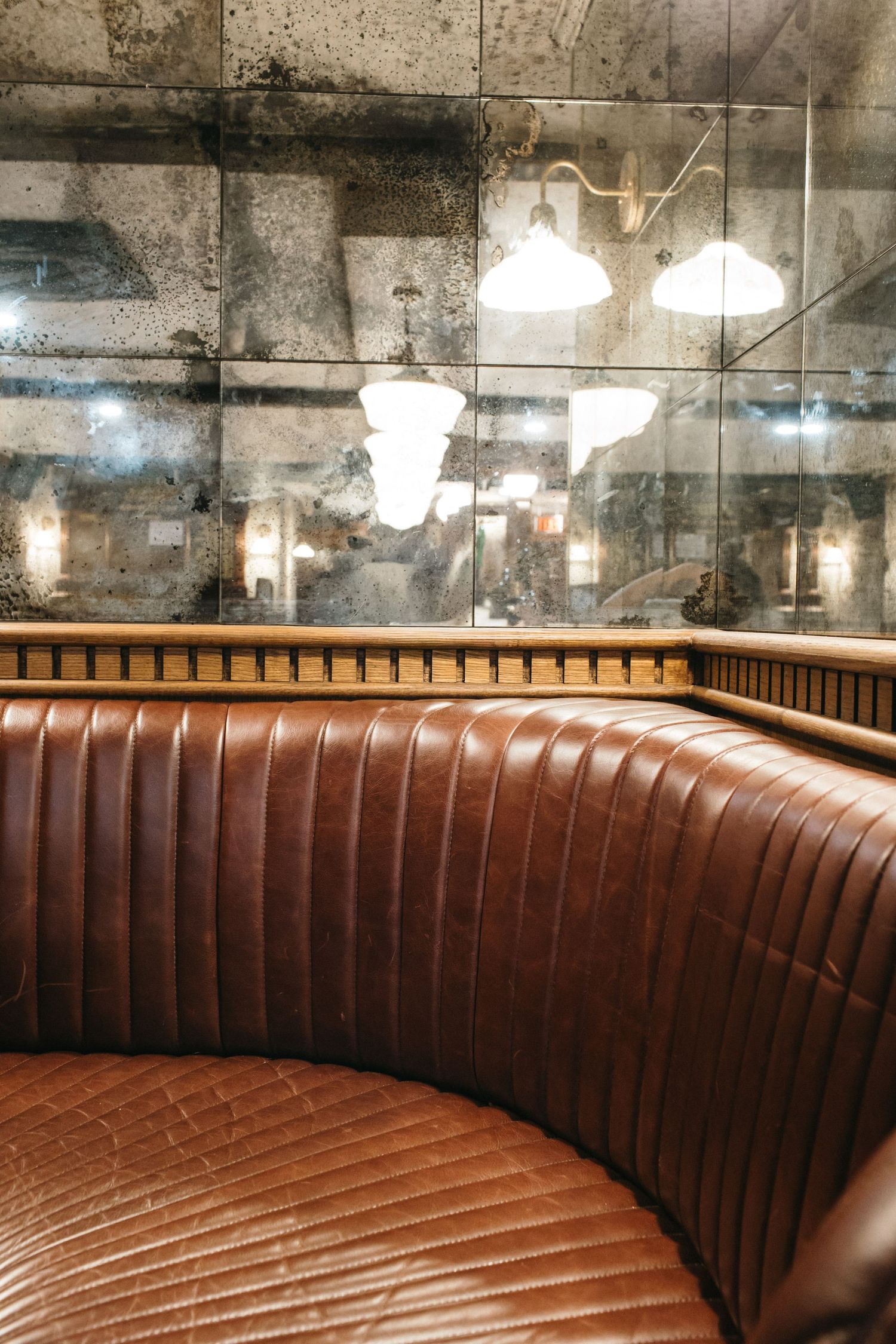 Curved brown leather booth seating in a restaurant with antique mirrored walls reflecting warm pendant lights.