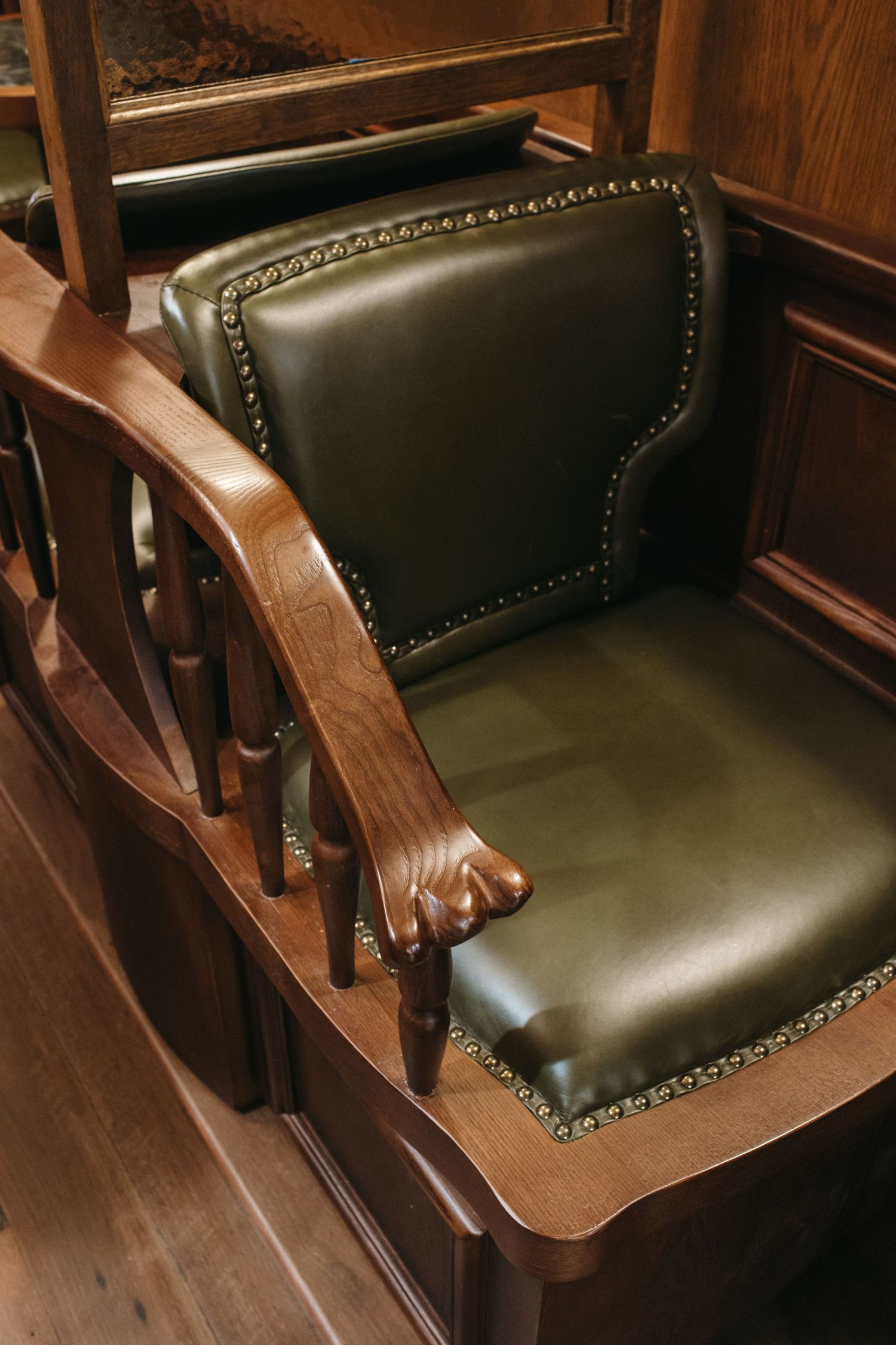 Elegant green leather courtroom chair with brass nail head trim and dark wood arms on hardwood floor.